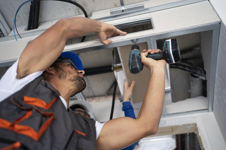 Worker installing ceiling with a drill.