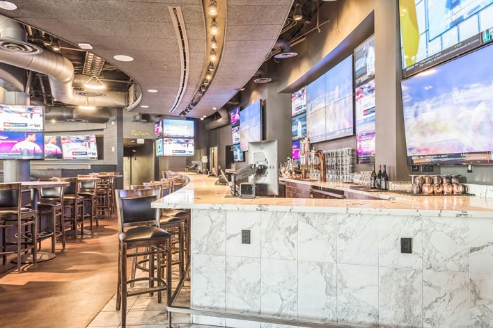 Modern sports bar with high stools and multiple screens.