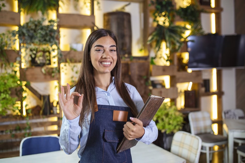 Happy waitress in restaurant giving OK gesture.
