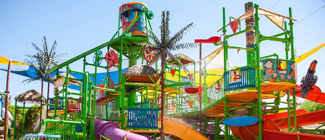 Colorful water playground with slides and palm trees.