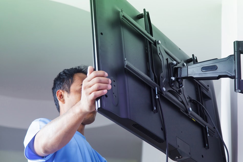 Technician installing flat screen TV on wall mount.