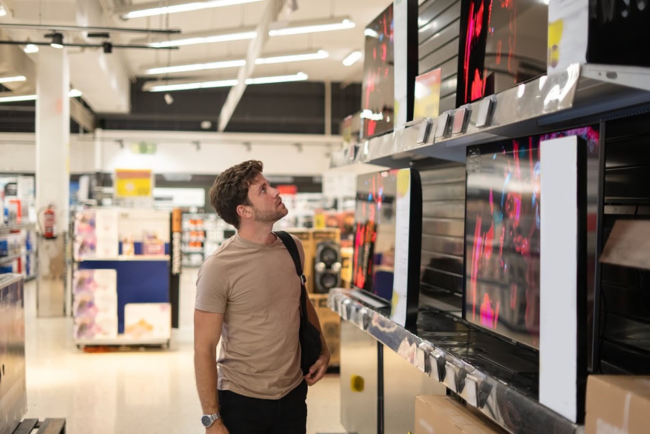 Man shopping for televisions in electronics store.