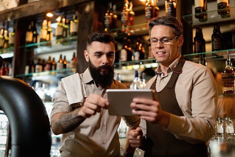Bartenders discussing drinks using tablet in bar