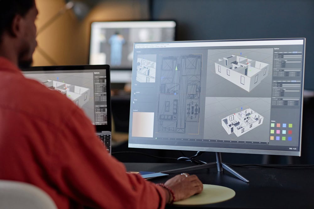 Person designing 3D floor plans on computer monitors.