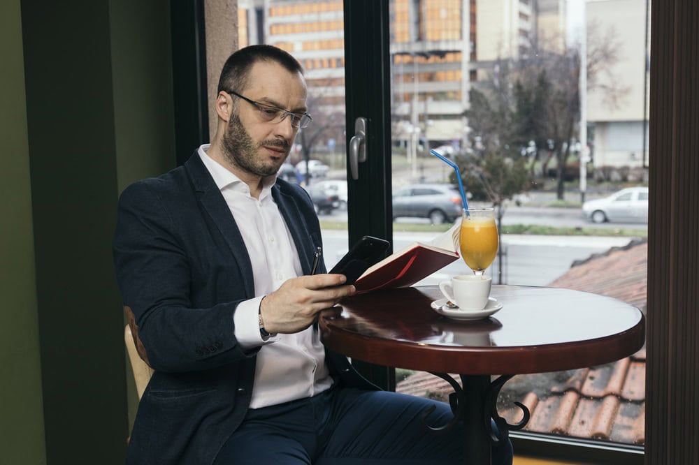 Man reading, phone in hand, at café table.