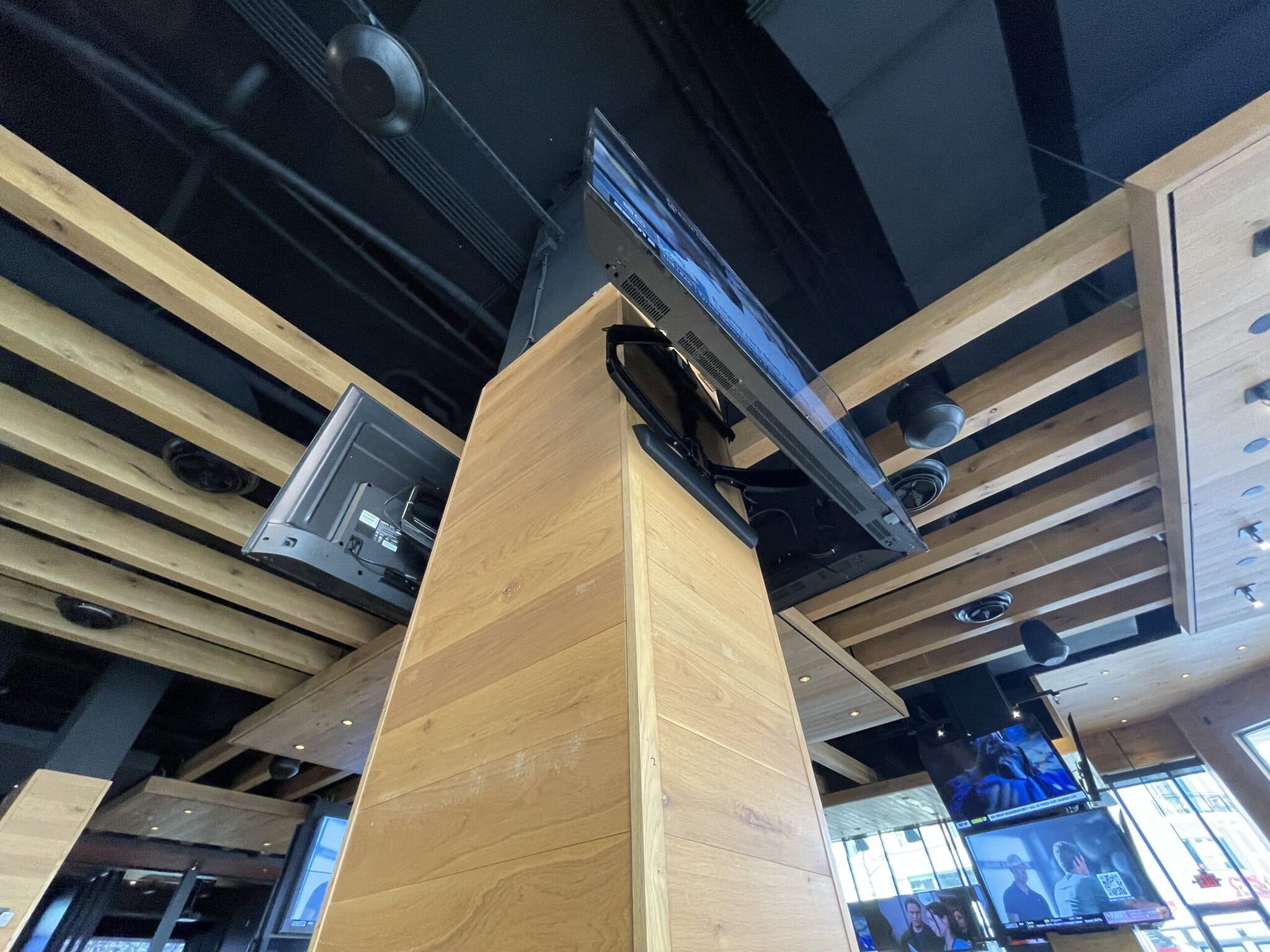 Televisions mounted on wooden ceiling in modern building.