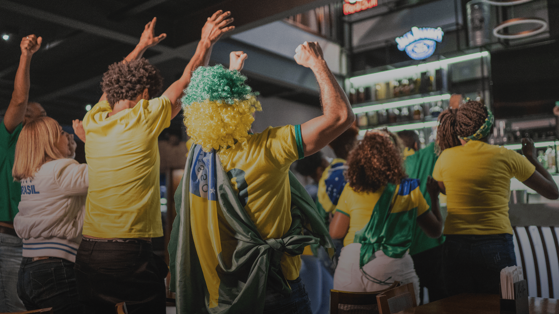 Brazilian football fans celebrating and cheering at a sports bar, wearing yellow jerseys and colorful wigs, showing excitement and team spirit.